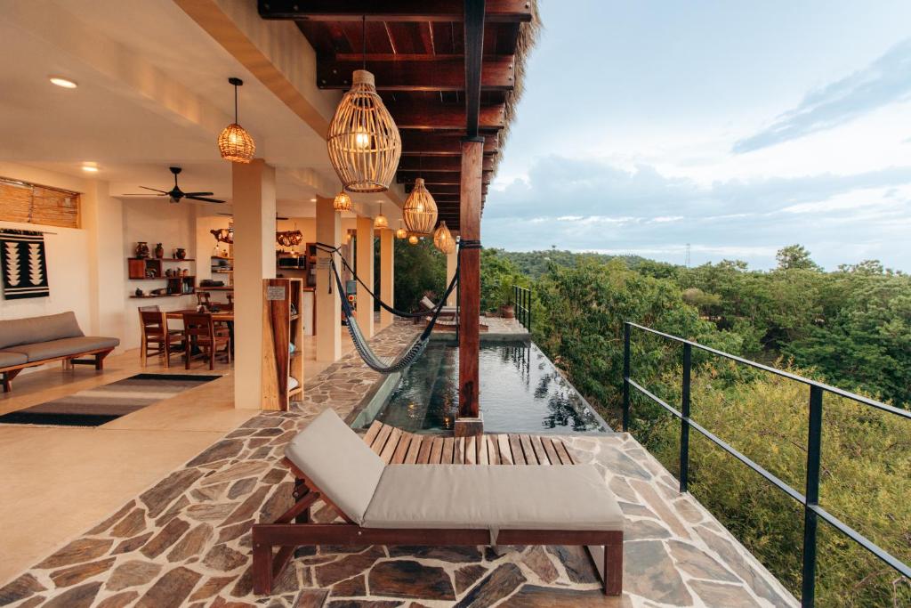Outdoor villa terrace with woven lanterns, a hammock, and a stone deck, overlooking a forested valley by an infinity pool.