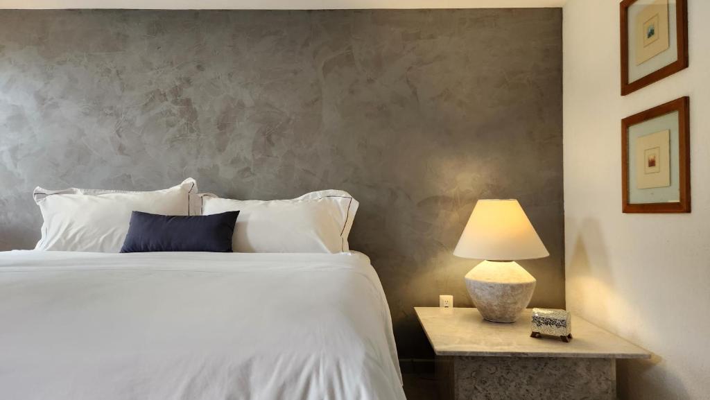 King-size bed with white linens and a navy accent pillow against a gray textured wall; a lit lamp sits on a marble nightstand to the right.