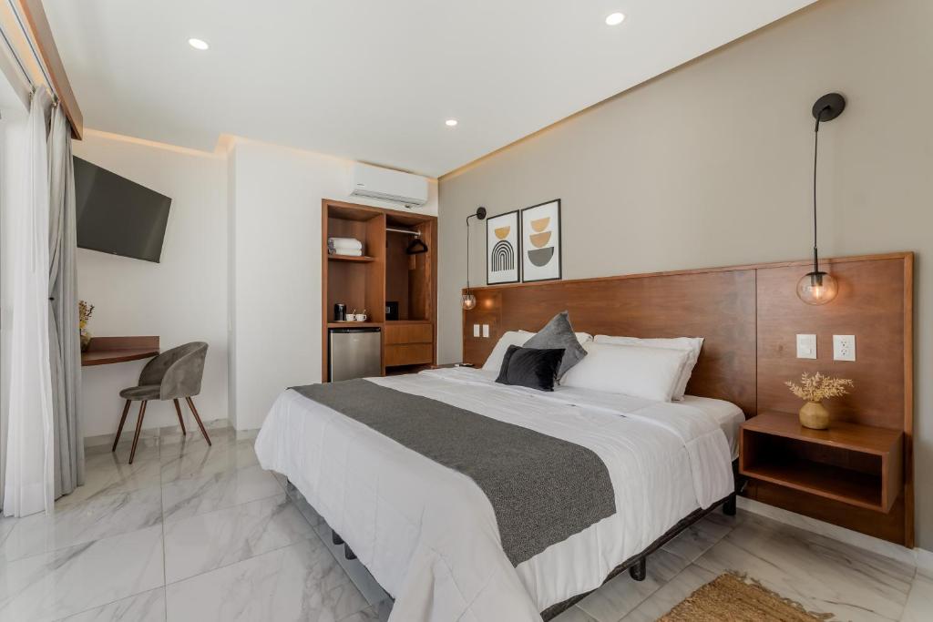 Modern hotel room with a large bed, white linens, gray throw, and a wooden headboard flanked by pendant lights and nightstands at each side.