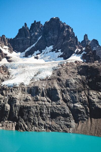 Jagged dark mountains with patches of snow above a blue glacier and turquoise lake at the base.