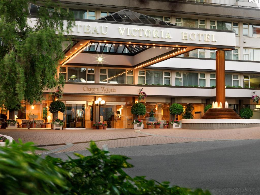 Entrance to Chateau Victoria Hotel with a lit canopy, glass doors, and potted plants outside the lobby