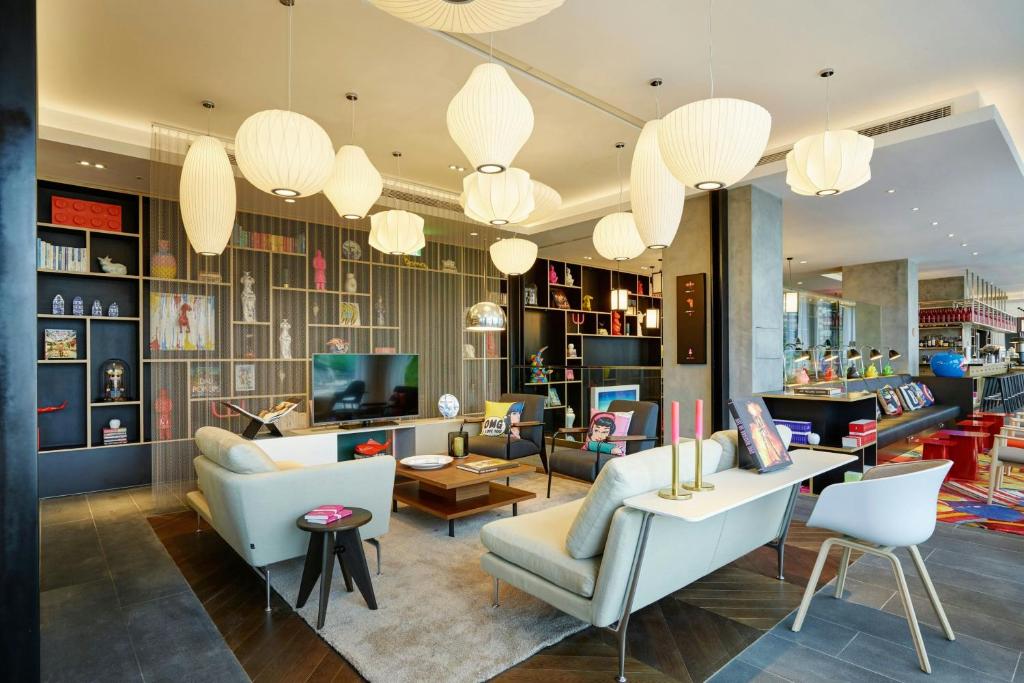 Contemporary hotel lounge with white sofas, a wooden coffee table, and a wall of shelves filled with decor and art.