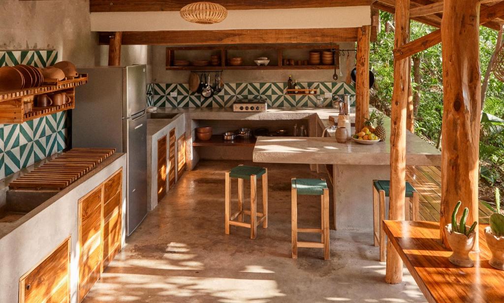 Rustic outdoor kitchen with concrete countertops, wooden cabinets, and a central island with three green-stool seats and a fruit bowl nearby.