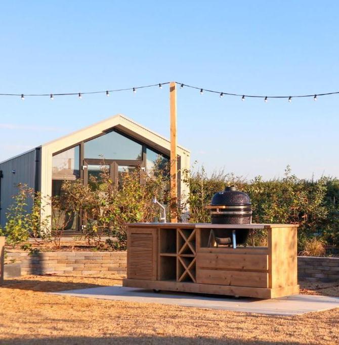 Outdoor wooden bar with built-in grill and wine rack in a backyard, string lights overhead.
