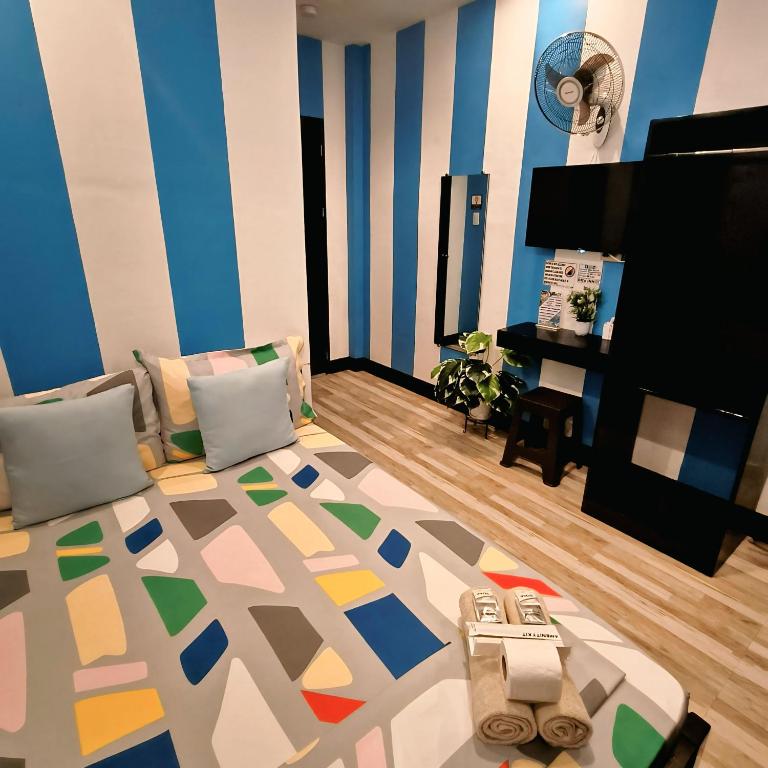 Hotel room with blue and white vertical striped walls, and a colorful geometric bedspread with pastel cushions.