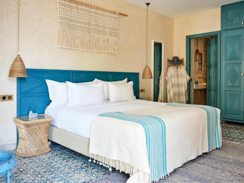 King-size bed with white linens and turquoise-striped throw in a bright room with wicker lamps and a blue headboard.