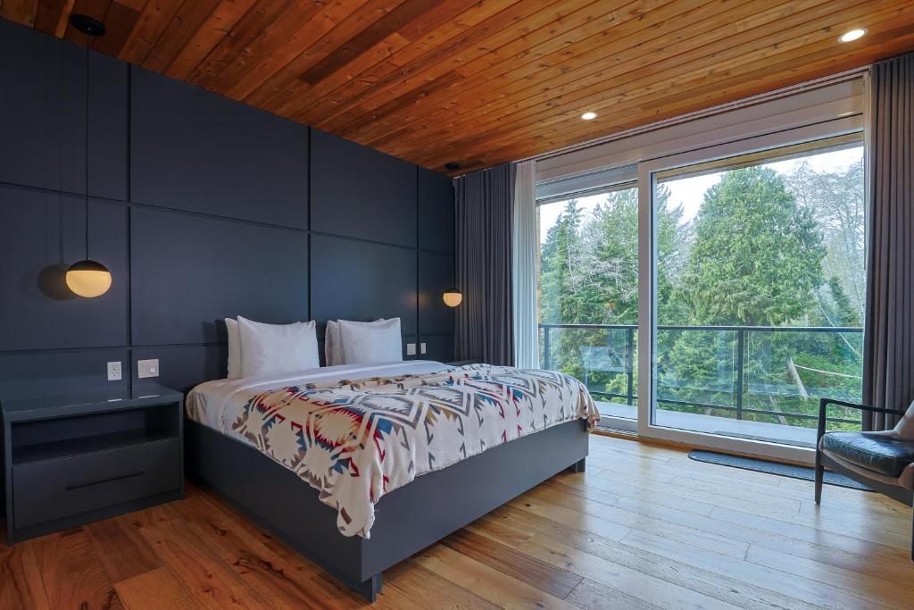 King bed in a modern blue-accent bedroom with dark headboard panels, bedside tables, and a large glass door to a balcony overlooking trees
