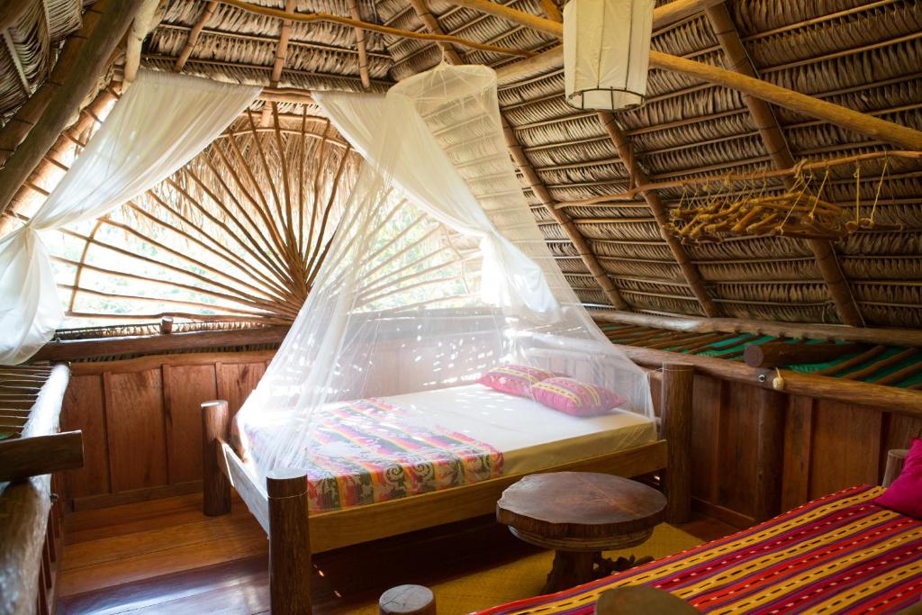 Bedroom inside a rustic thatched hut with a canopy bed, white mosquito net, and colorful patterned linens.