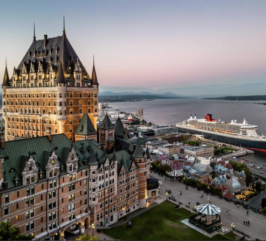 Château Frontenac hotel along the riverfront at sunset with a large cruise ship docked nearby.