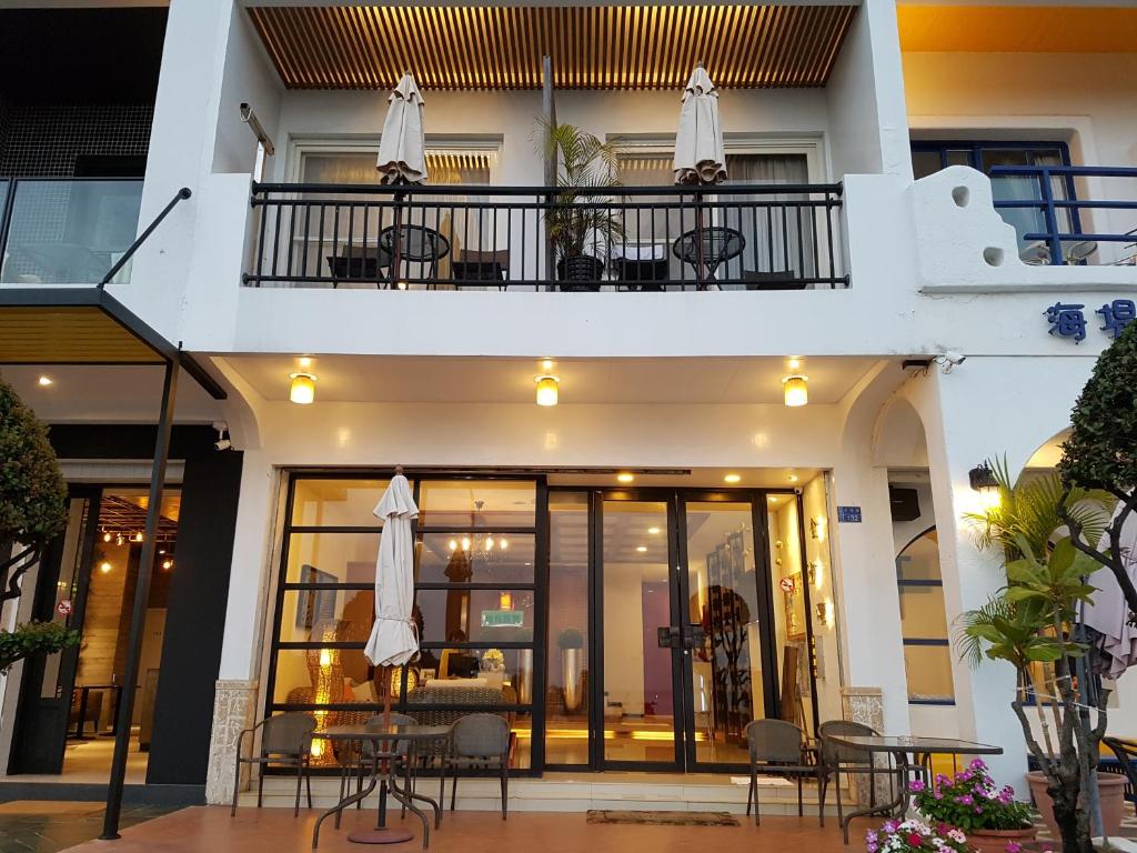 White, two-story restaurant with glass storefront and outdoor seating; warm interior lighting visible through windows and a balcony with tables and umbrellas.