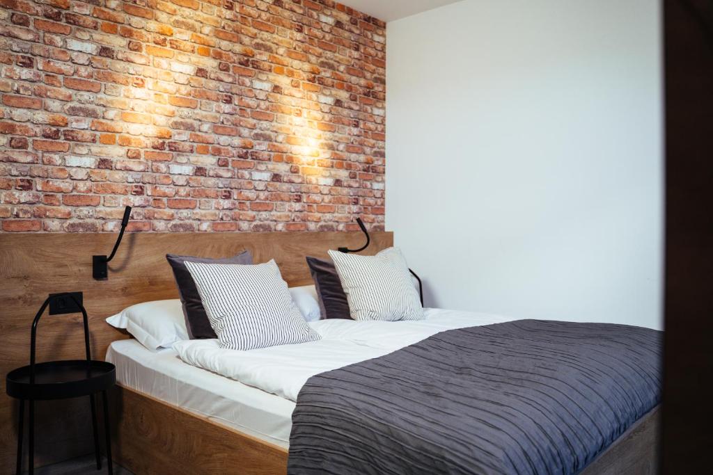 Hotel bedroom with a brick accent wall, wooden headboard, white linens, and two striped pillows with a gray quilt.