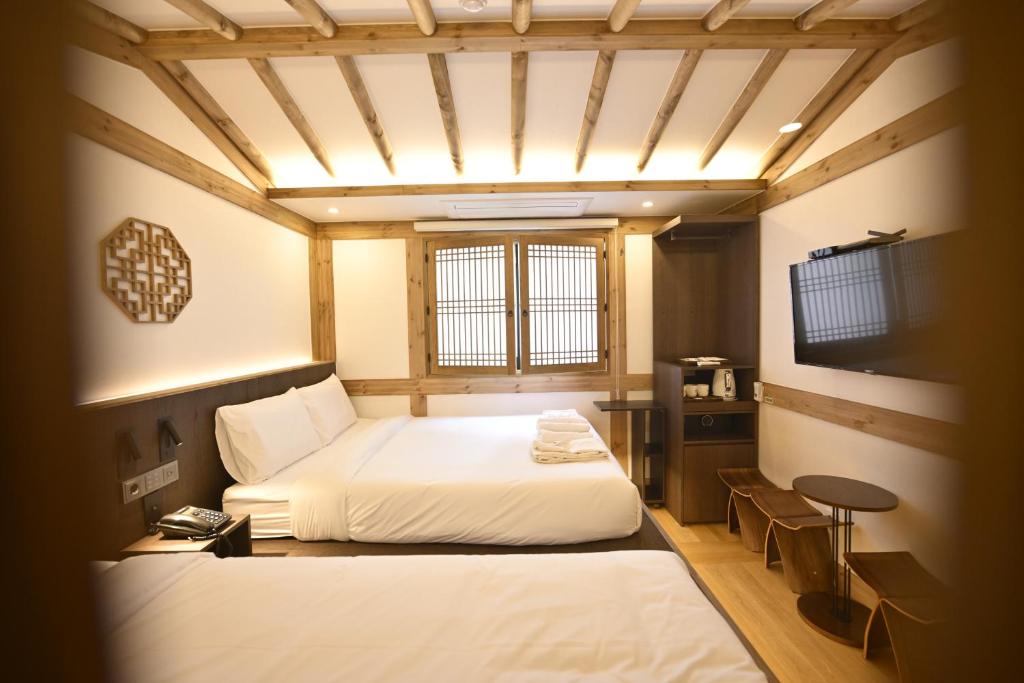 Hotel room with two white beds, wood beam ceiling, and a wall-mounted TV
