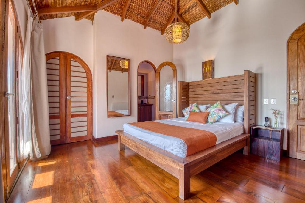 Wooden bedroom with a low platform bed, orange bed runner, and tropical pillows on warm wood floors