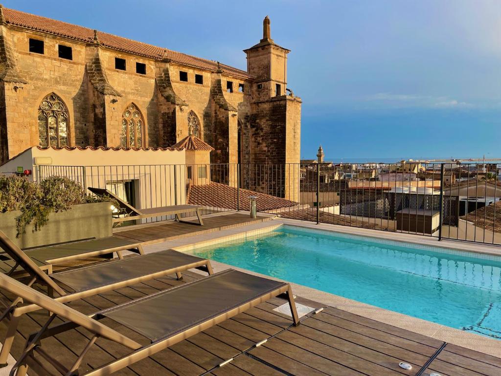 Rooftop pool with wooden deck and brown lounge chairs beside a historic stone building with arched windows.