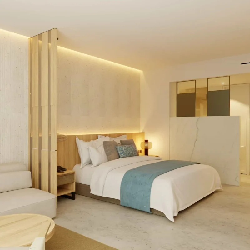 Modern hotel bedroom with a low platform bed, white linens, teal throw, and soft backlit headboard lighting. Stylish divider and seating area adjacent.