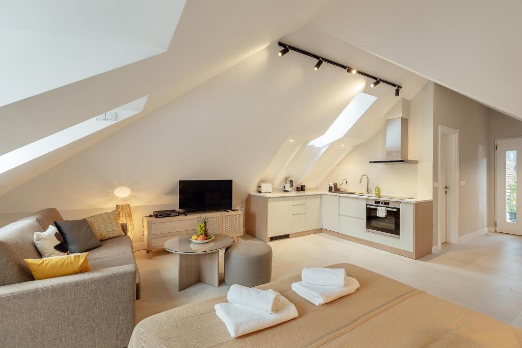 Bright open-plan loft with a gray sofa, round coffee table, TV, and a compact kitchen under a sloped ceiling.