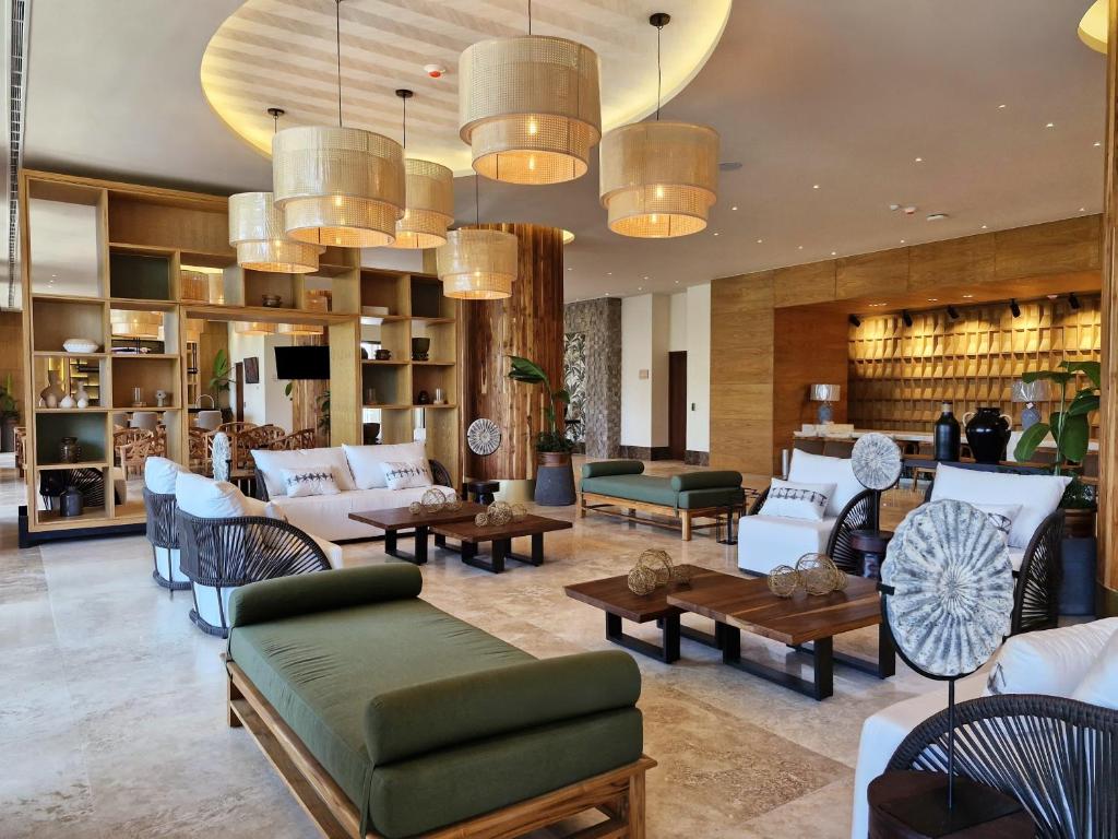 Luxurious hotel lobby with green-cushioned benches, white sofas, wooden coffee tables, and large woven pendant lights.