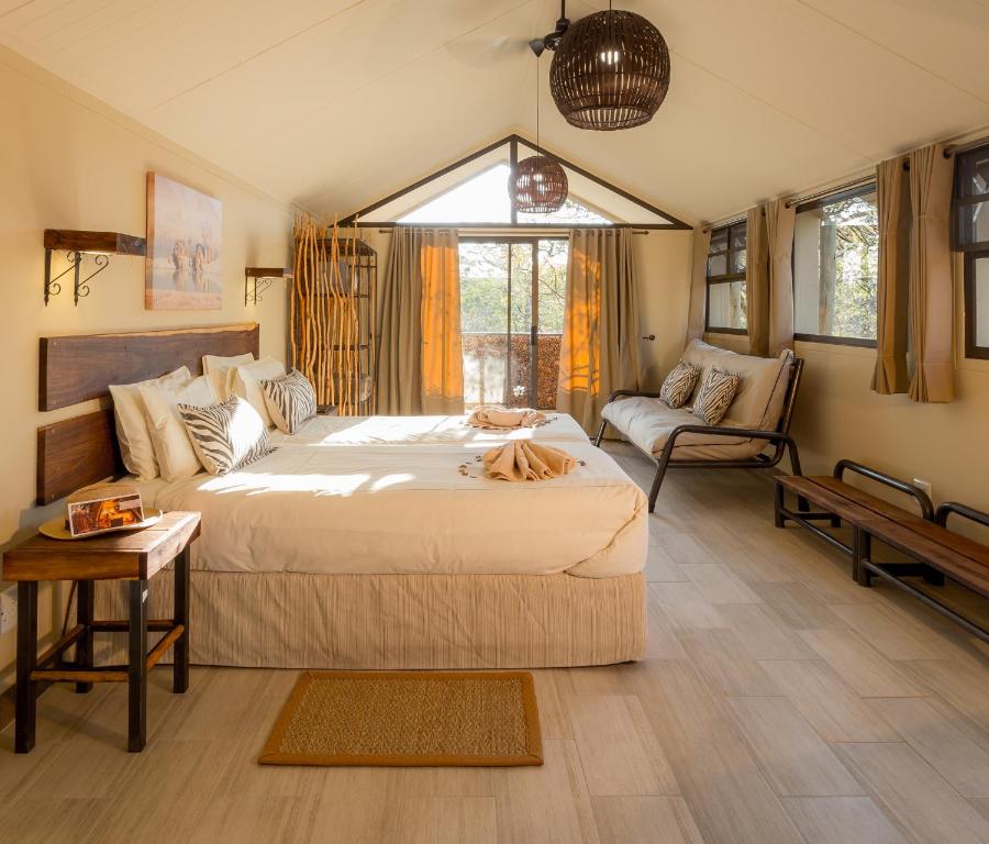 Rustic hotel bedroom with two large beds, beige linens, and a seating area by windows with wicker pendant lights.