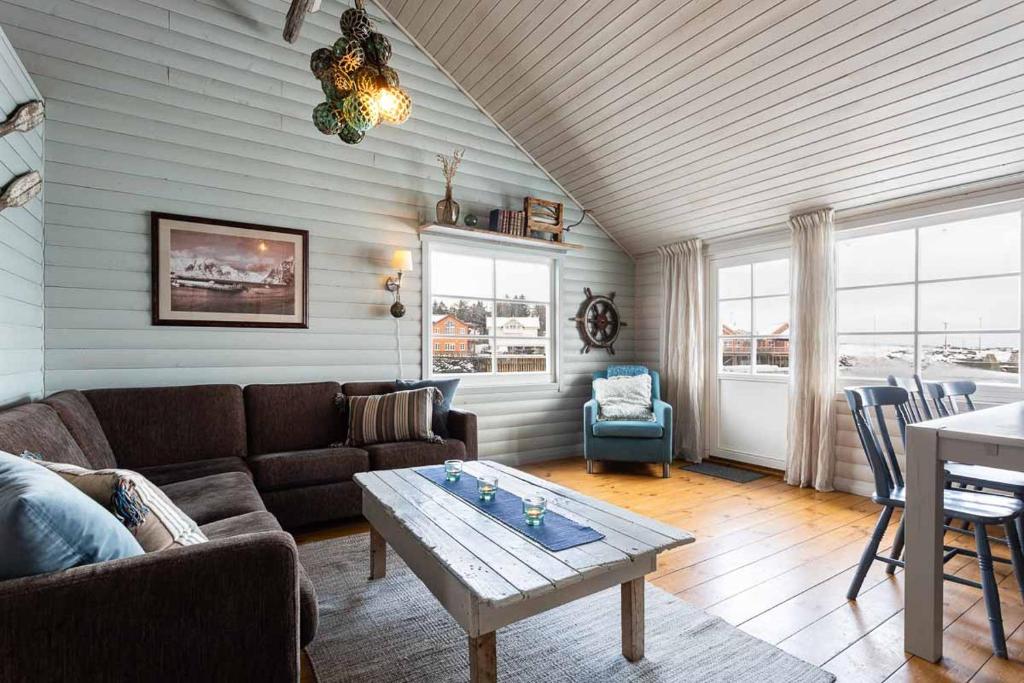 Cozy coastal living room with a brown sectional, light blue paneled walls, and a white distressed coffee table by large windows showing a harbor view.
