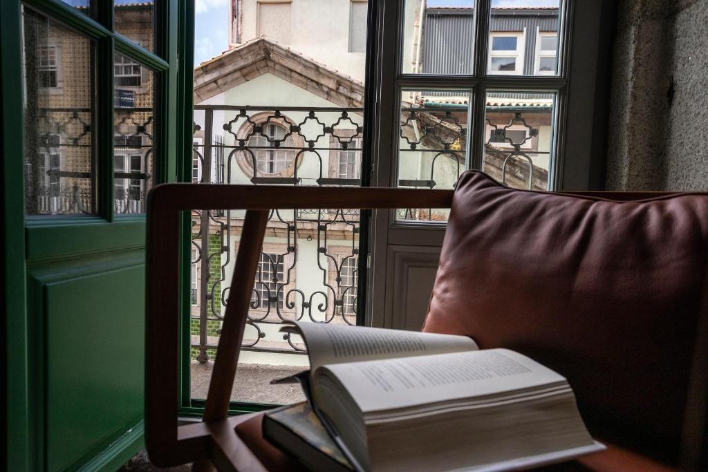 Open green window with a brown leather chair and an open book resting on its arm, overlooking an ornate metal balcony outside.