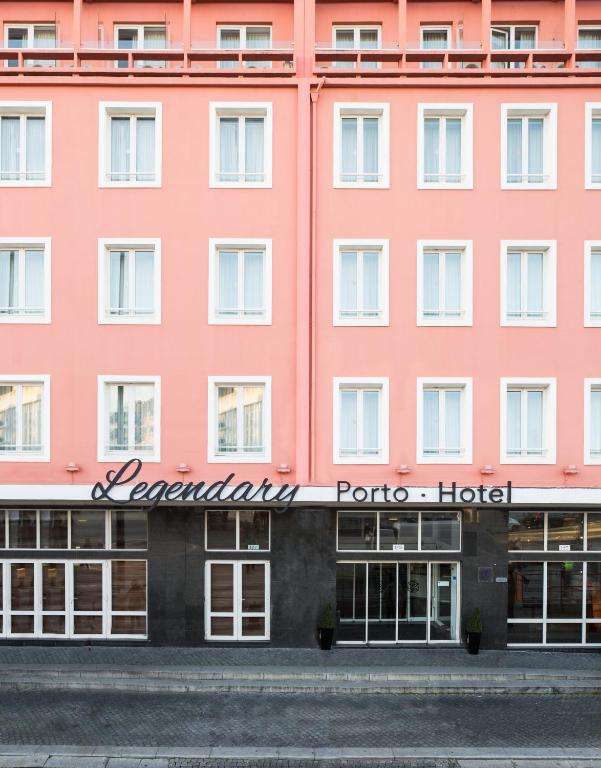 Facade of a pink hotel with white-framed windows and a black base, ground-floor glass doors, and a sign saying 'Legendary Porto Hotel' beneath the windows.