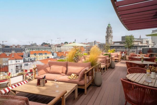 Rooftop lounge with pink cushions and wooden furniture overlooking a city skyline with a tall clock tower in the distance.
