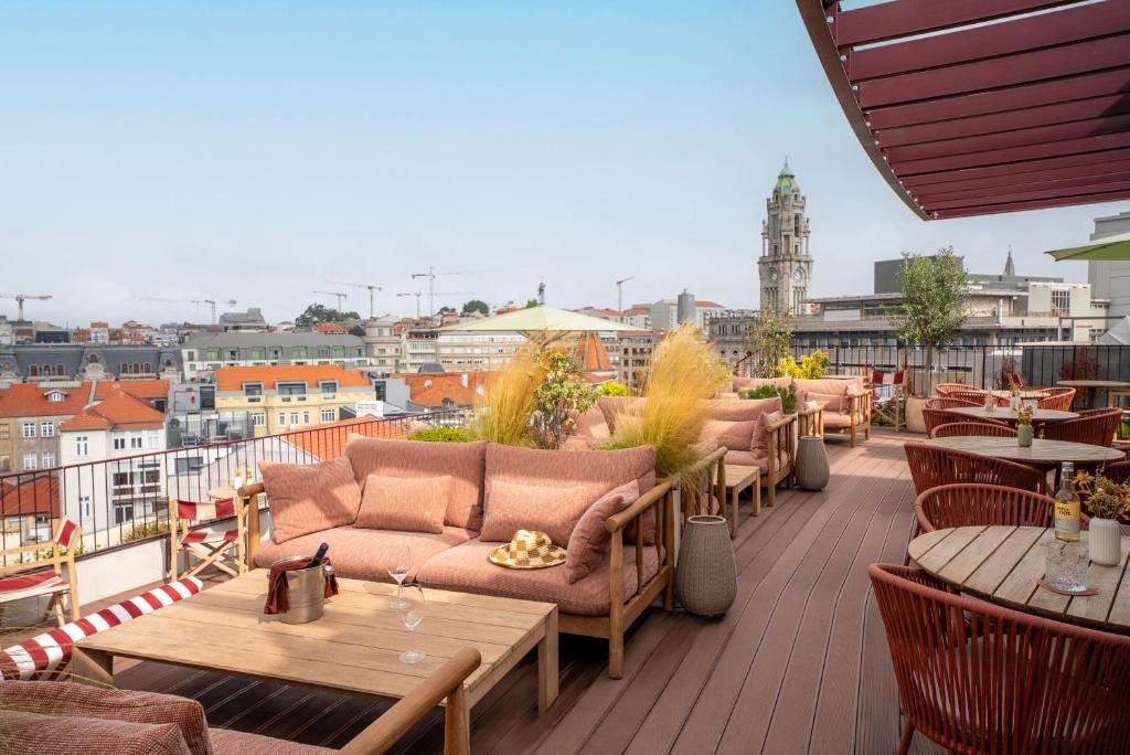 Rooftop lounge with pink cushions and wooden furniture overlooking a city skyline with a tall clock tower in the distance.