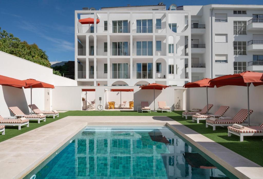 Rectangular pool area with blue water, white loungers, and red umbrellas under a clear sky.