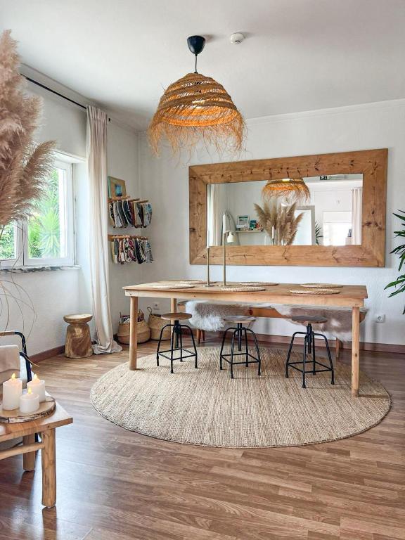 Boho-inspired dining/studio space with a long wooden table, black stools, and a circular jute rug, plus a large wooden-framed mirror and a woven pendant light above.