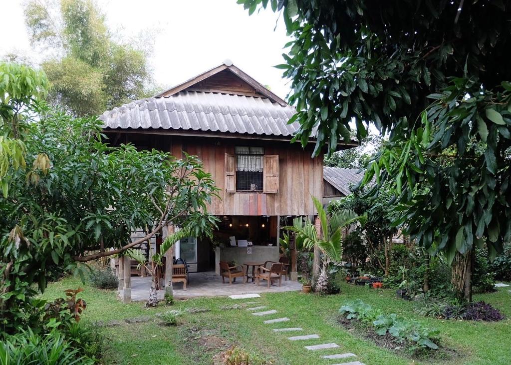 Wooden two-story cabin with a shaded patio and outdoor seating among lush tropical plants.