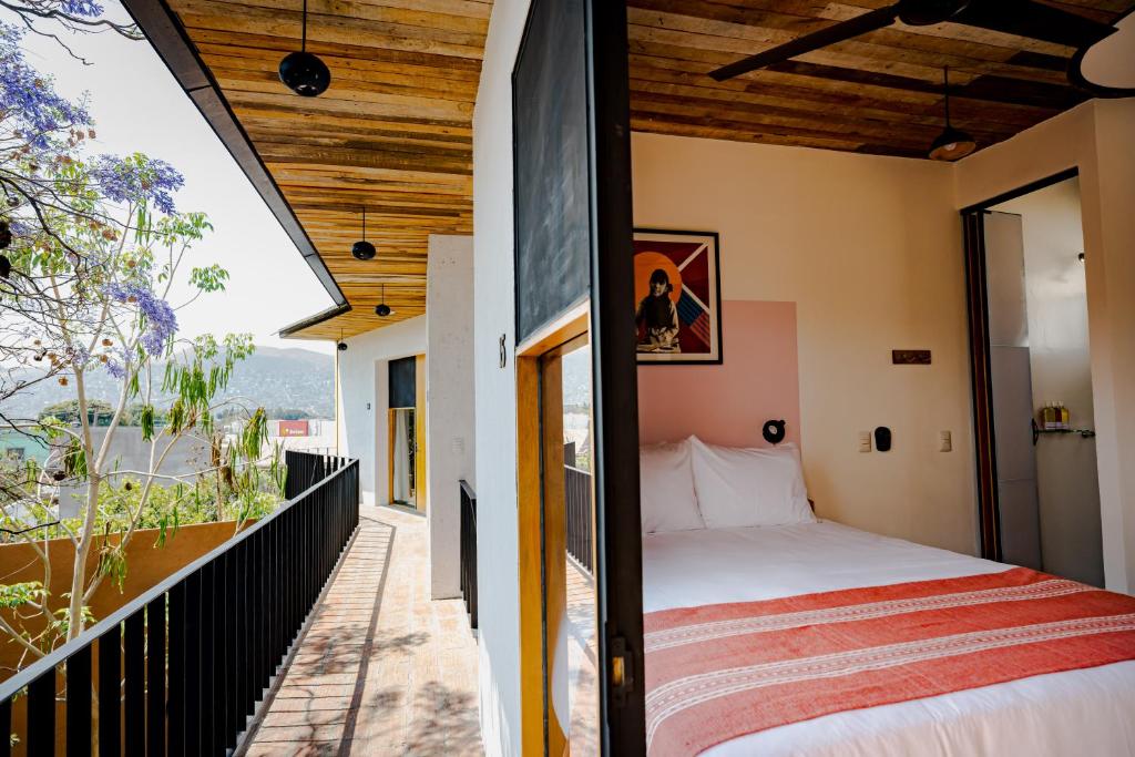 Hotel bedroom with white linens and an orange striped throw, open door to a wooden balcony overlooking hills.