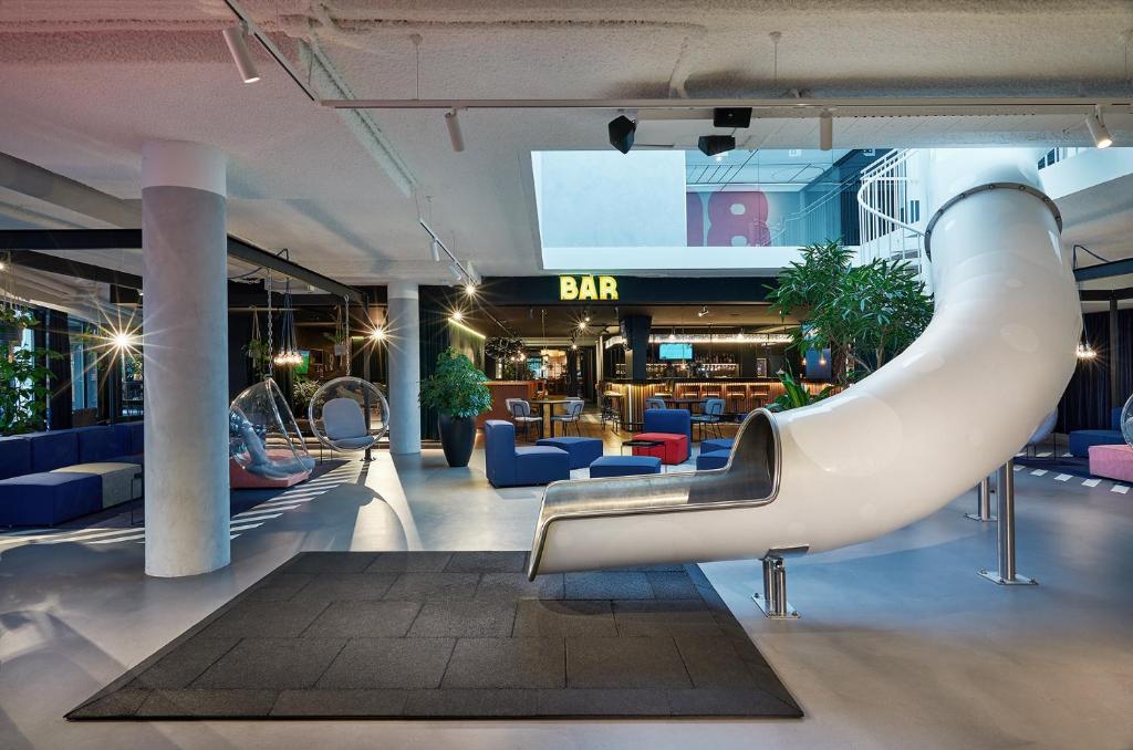 Indoor lounge with a large white curved slide, blue seating, and a dimly lit bar area in the background