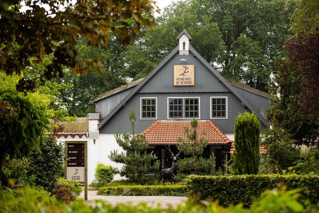 Grey wooden hotel with a red-tiled roof surrounded by trees and a manicured garden.