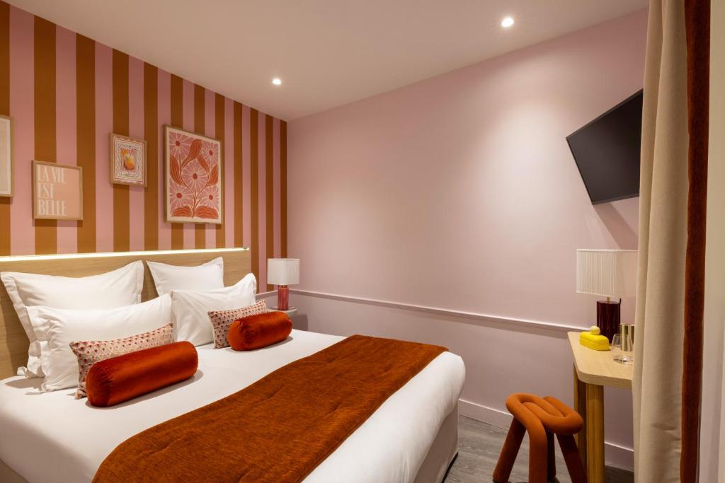 Hotel room with a plush bed, white linens, orange bolsters, and a pink striped accent wall.