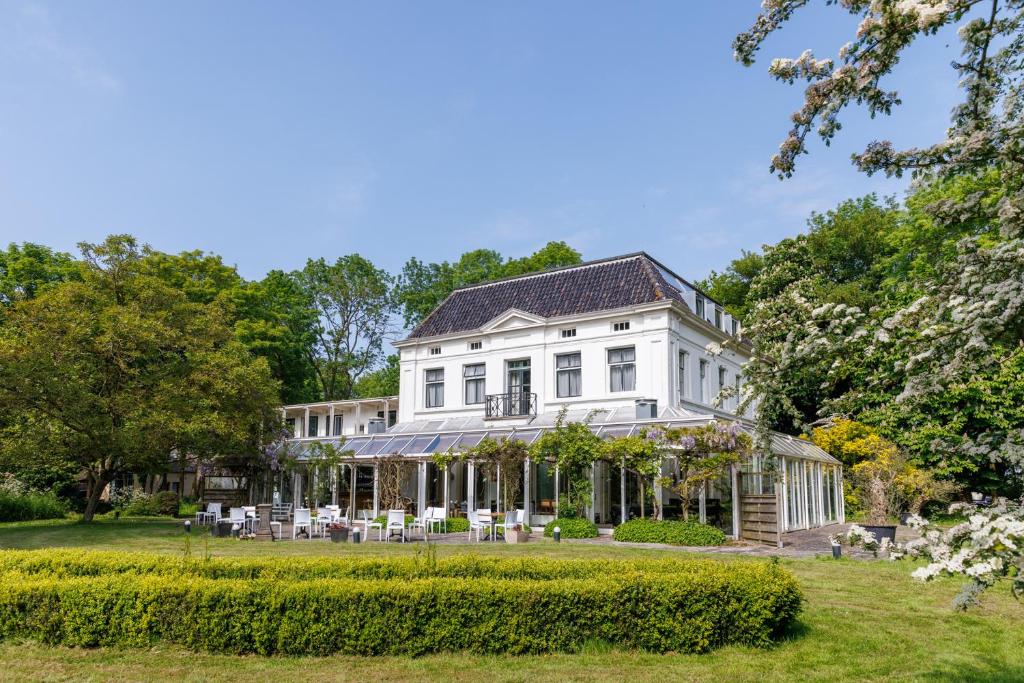 White two-story house with a glass conservatory and well-kept garden on a sunny day.
