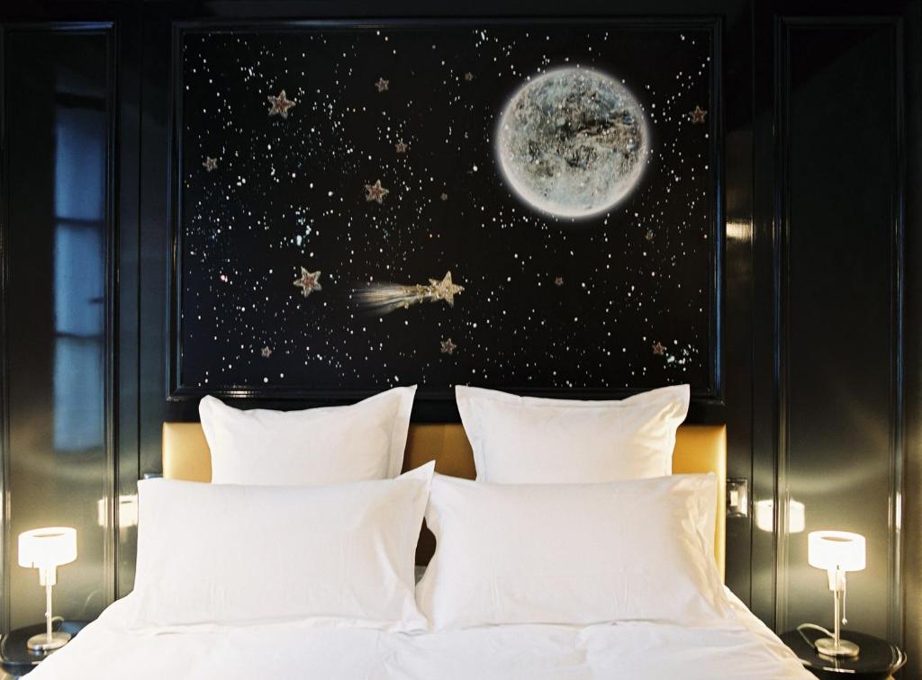 Bed with white linens in a dark-paneled room, space mural featuring the moon and stars above the headboard wall.