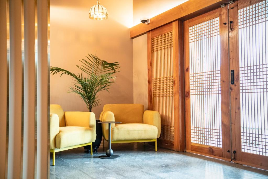 Bright lounge area with two yellow armchairs, a small round table, and a tall palm near wooden lattice doors.