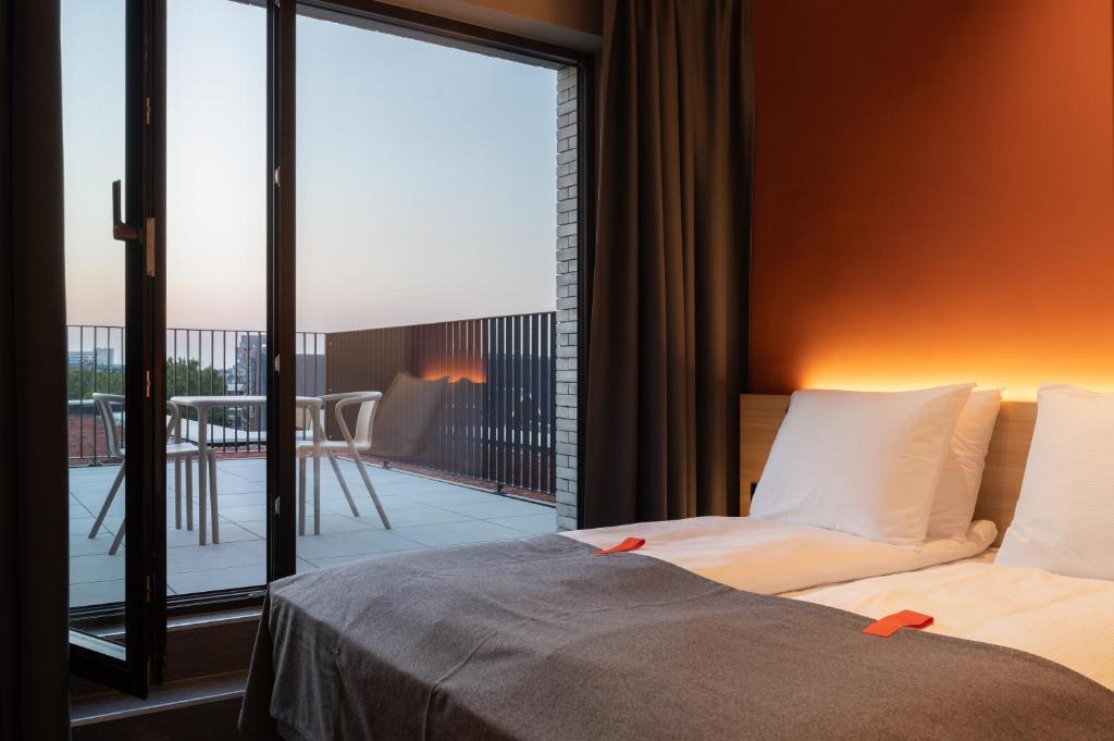 Hotel room with balcony; bed has two pillows and warm lighting, open glass door to a patio with a table and chairs.