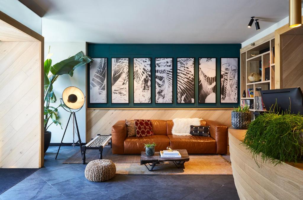 Modern living room with a brown leather sofa, black-and-white framed art panels, and a tall floor lamp on a patterned rug amid greenery.