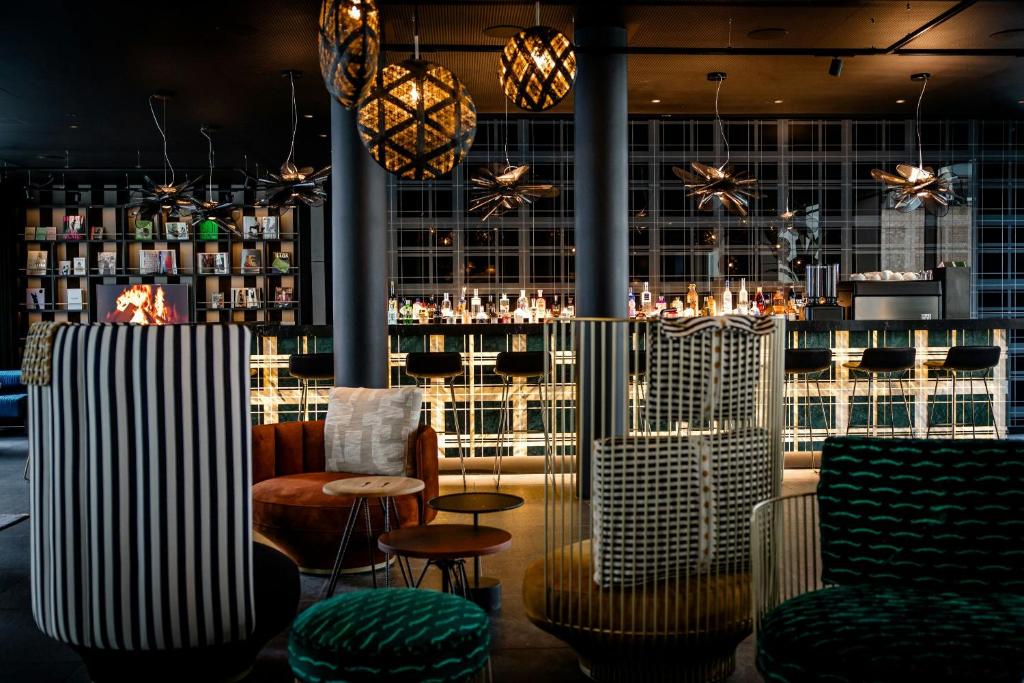 Modern bar lounge with striped high-back chairs, round stools, and a backlit bottle-bar counter across the room.