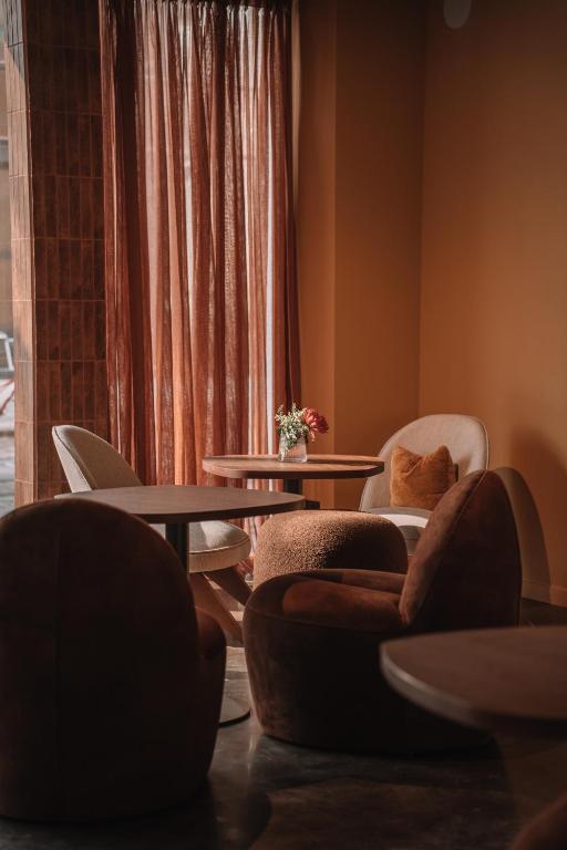 Cozy cafe seating with round tables and plush brown chairs by a window with rust-colored curtains; small vase of flowers on the table.