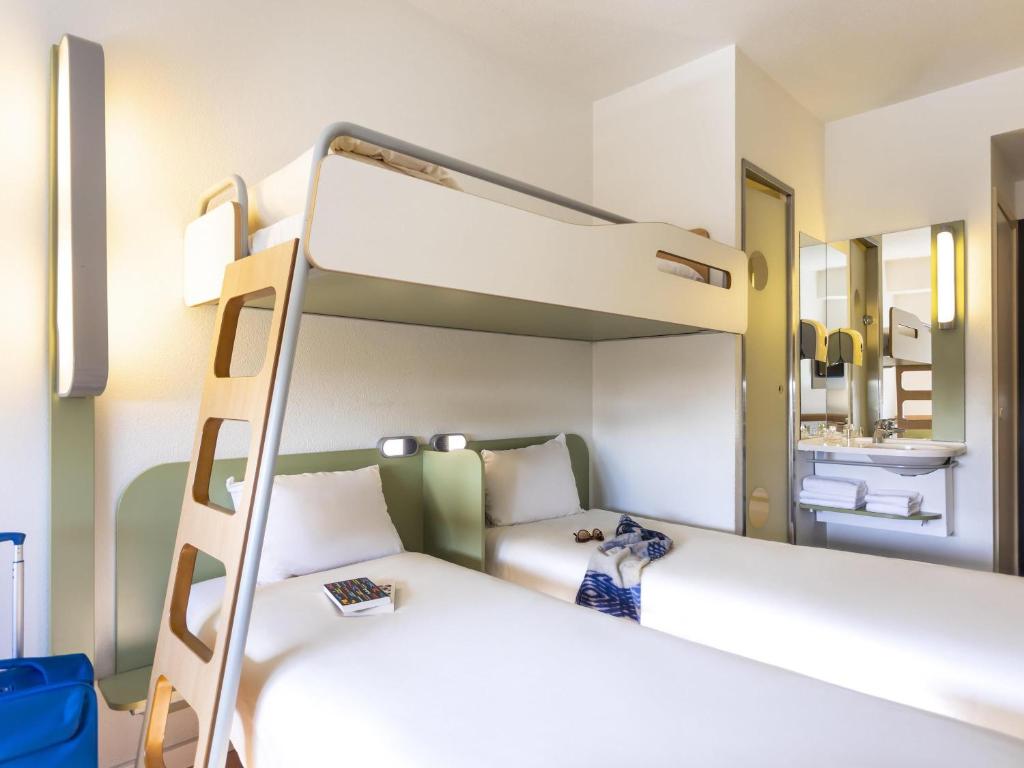 Hotel room featuring a top bunk over two single beds, with a wooden ladder and white bedding outside the bathroom area.