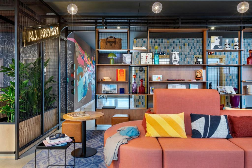 Cozy modern lounge with an orange sofa, colorful cushions, and open shelving in a stylish workspace in the background.