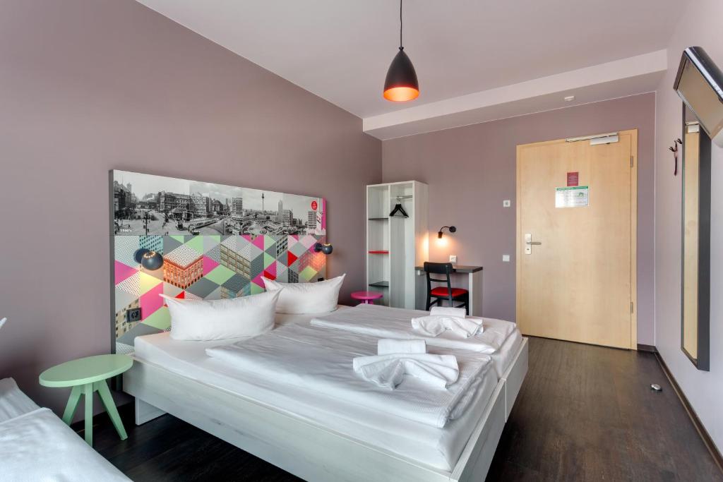 Large hotel room with a white bed, colorful geometric headboard, and a green round side table by the wall.