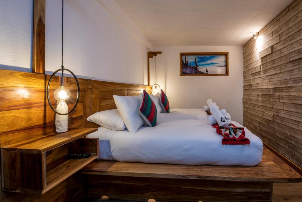 Wood-paneled hotel bedroom with a large white bed, colorful pillows, and warm pendant lighting; framed beach photo on the far wall.