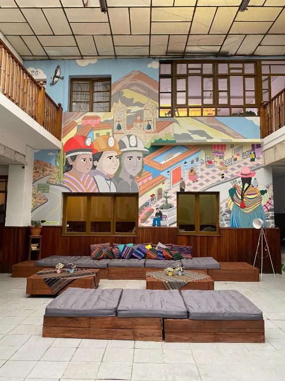 Indoor courtyard with a large colorful mural of miners, mountains, and village scenes behind wooden seating with gray cushions and colorful pillows.
