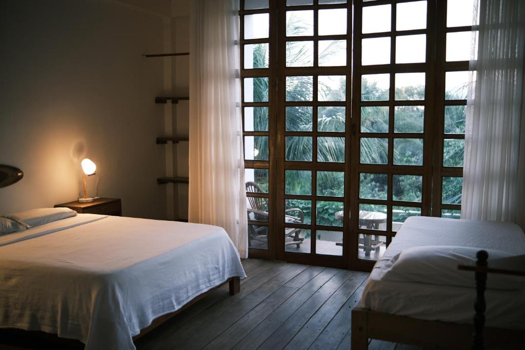 Bedroom with two beds, warm bedside lamp, and large wooden-framed glass doors opening to a balcony outside.