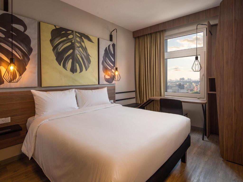 Hotel bedroom with a large white bed, wooden headboard, and three leaf-themed canvas prints above the headboard