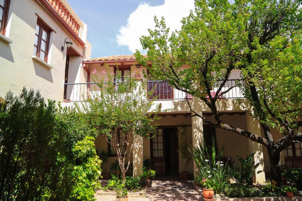 Two-story beige courtyard house with red-tiled roof, balconies, and leafy trees casting shadows on the walkway.