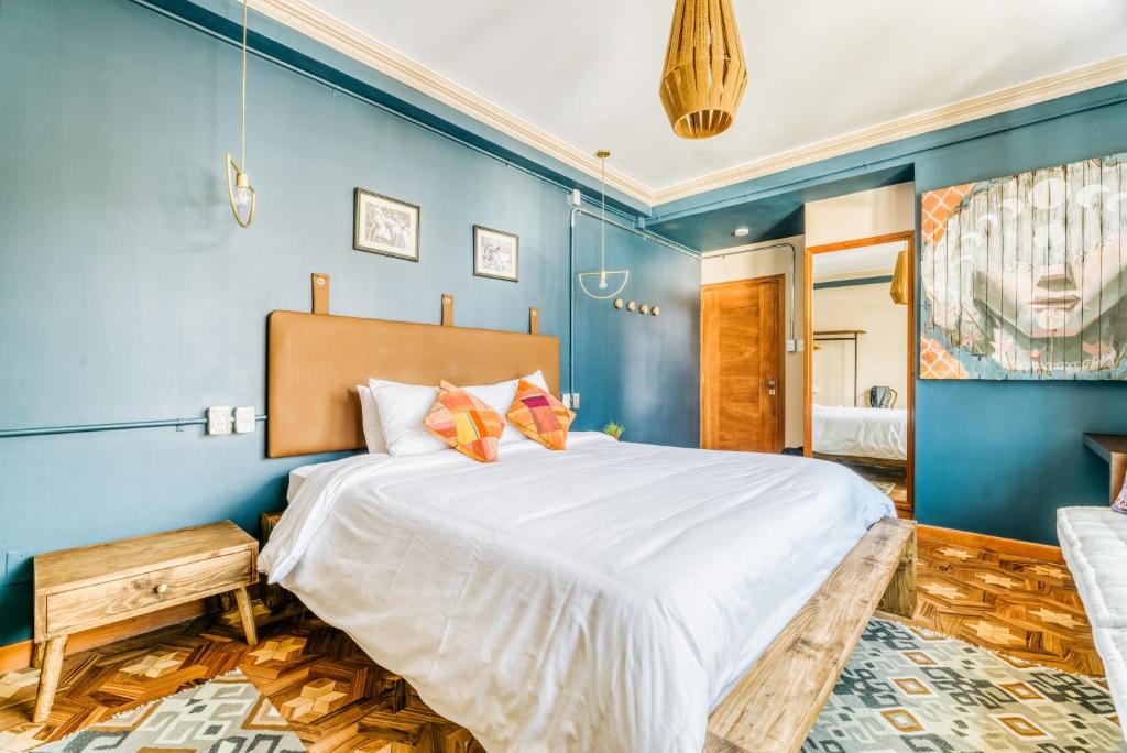 Blue-walled hotel room with a large white-bed, wooden bench footboard, and matching nightstands on a patterned rug.